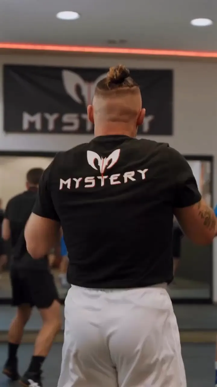 Trainer im Mystery-Shirt vor dem Banner in der Halle